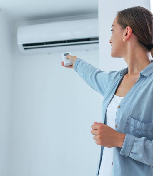 Young woman adjusts the temperature of the air conditioner using the remote control in room at home